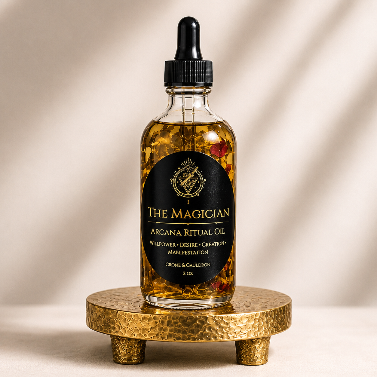 A clear glass dropper bottle of The Magician Arcana Ritual Oil filled with golden liquid and dried botanicals, displayed on a small hammered gold stand against a warm beige background.