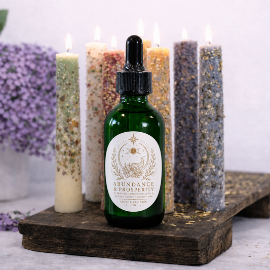 A dark green glass dropper bottle labeled 'Abundance & Prosperity' sits on a rustic wooden board, surrounded by lit decorative candles in neutral and earthy tones against a soft light background.