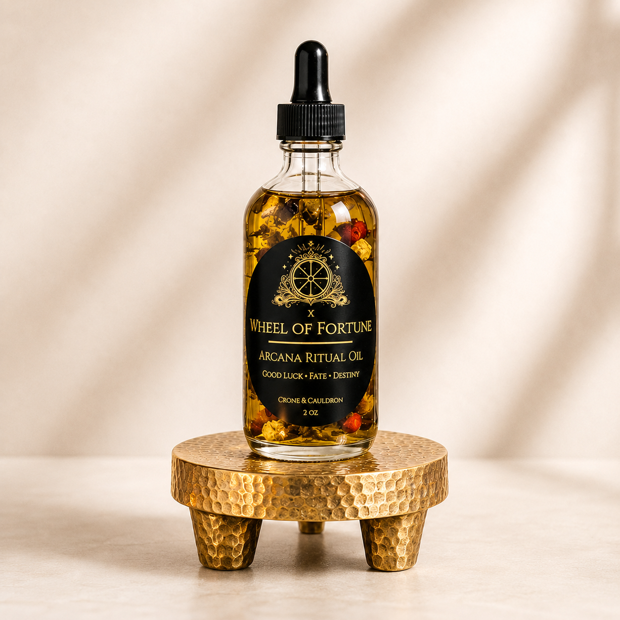 A 2 oz glass dropper bottle of Wheel of Fortune Arcana Ritual Oil by The Arcane Society, filled with golden oil and dried herbs, displayed on a textured gold stand against a warm beige background.